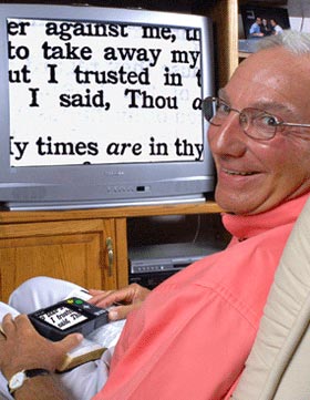 Image of older man using his opal hooked up to his television set with the magnified image showing on the TV.